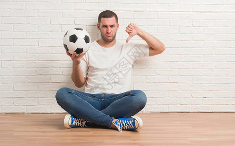 坐在白砖墙旁的年轻caucasian男子拿着足球图片