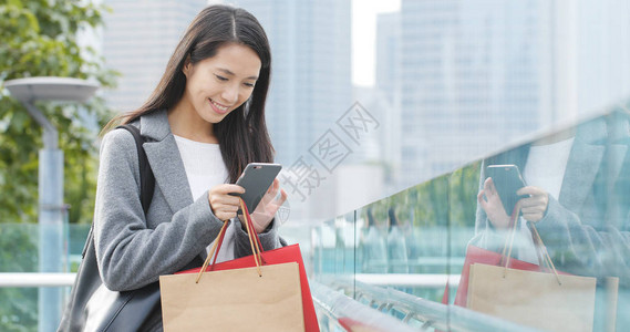 女人在户外看手机提着购物袋图片