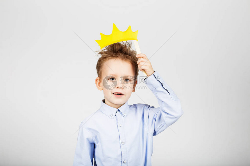 一个逗人喜爱的小男生的画象有黄色纸冠的反对白色背景快乐微笑的孩子与有趣的照片道具回到学校孩图片