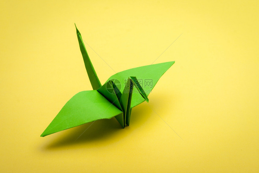 黄纸背景上的绿色折纸鹤图片