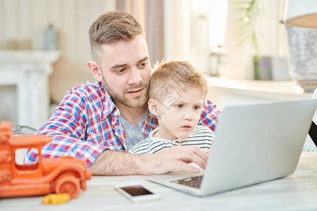 英俊父亲教儿子如何使用笔记本电脑或一起玩电脑游图片