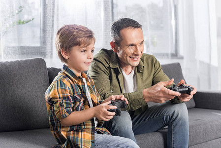 父亲和儿子坐在沙发上玩游戏纸板的游戏机图片