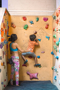 一个女人正在训练她的儿子男孩爬上攀岩墙妈帮助孩子训练教图片
