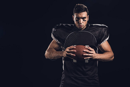 年轻自信的美国足球运动员手里拿着球看着在黑色上图片
