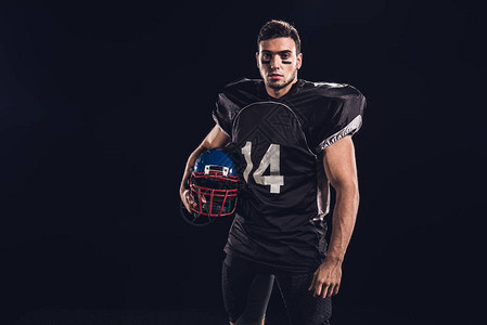 身穿黑色制服的美式足球运动员持有头盔图片