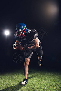 美国足球运动员拿着球站在黑色的聚光灯下图片