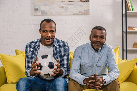 快乐的非洲美国父亲与成年的儿子拿着足球和微笑图片