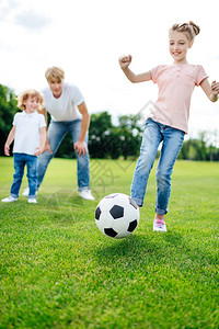看着可爱的小女孩在草地上踢足球在图片