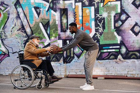 坐在轮椅上的老年残疾人和在街上一起打篮球的非裔美国男图片