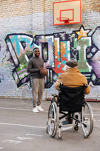 坐在轮椅上的老年残疾男子的背面观望着在街上打篮球的非图片