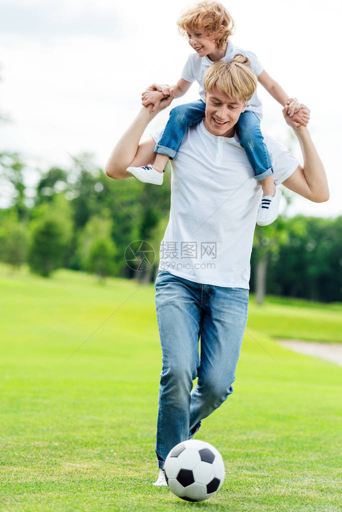 父亲在公园踢足球时背着小儿子肩图片