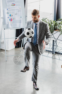 穿着正式服装的青年商人在办公室踢足球时全场观看图片