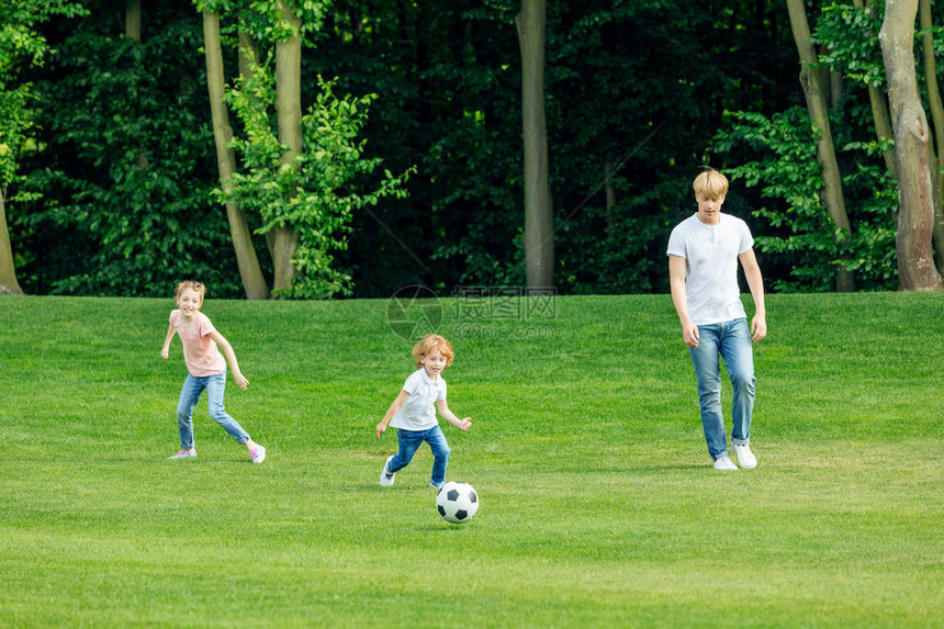 带着两个可爱的孩子在公园绿草坪上踢足球的年图片