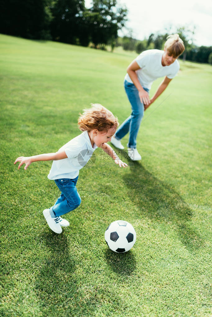 喜悦的父亲和儿子在公园踢足球的图片