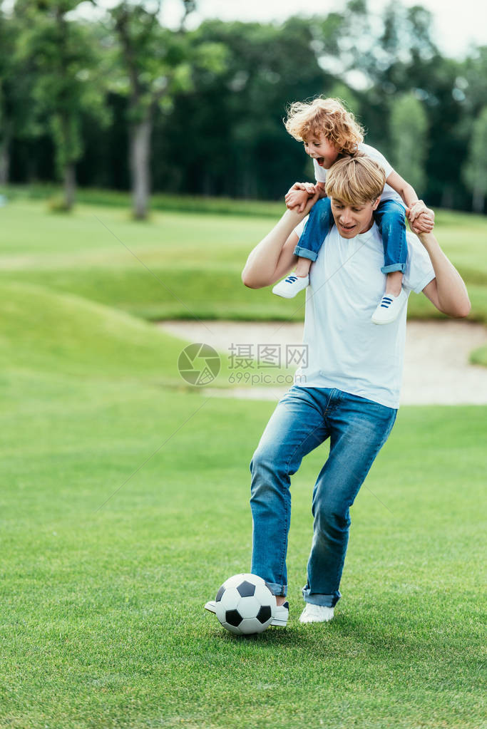 父亲在公园踢足球时背着小儿子肩图片