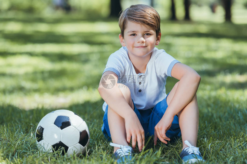 可爱的小男孩坐在草地上带着足球图片