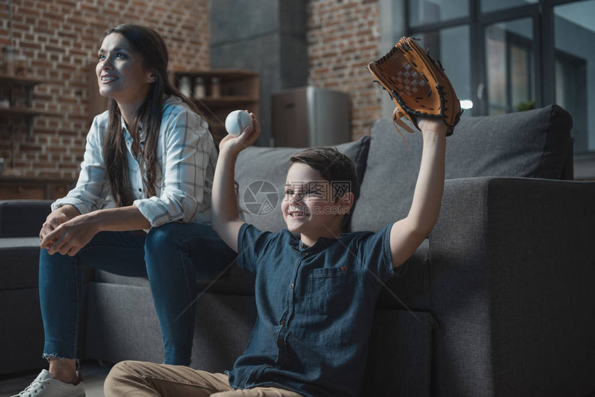 带着棒球手套和球的欢呼小男孩和妈坐在客厅图片