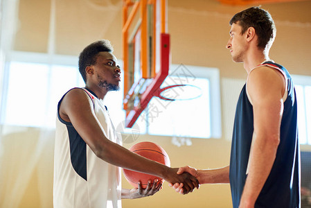 两个篮球运动员在比赛开始前站在法庭上握手的侧面景象图片