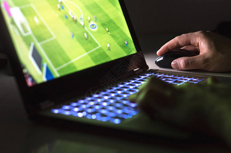 青年男子利用笔记本电脑在黑暗中或深夜在线踢足球或足球比赛图片