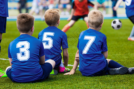 年轻足球队的孩子们身着蓝色运动制服的男孩作为预备队球员坐在足球场上图片