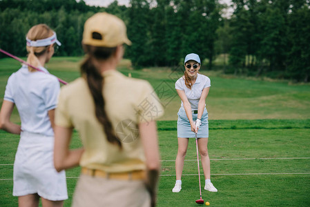 戴着高尔夫设备的戴帽子的女有选择地关注在高尔夫球场打高图片