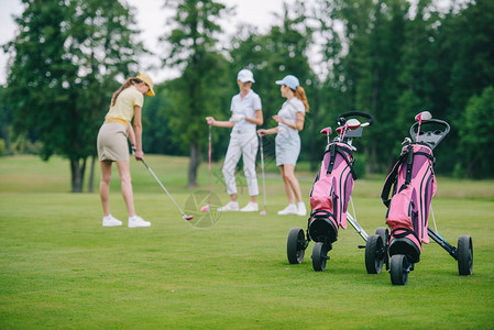 高尔夫装备的选择焦点带高尔夫球杆的戴帽子的女人和站在高尔夫球图片