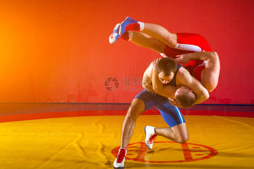 在健身房的黄摔跤地毯上穿着红制服和蓝制服摔跤的两位希腊图片