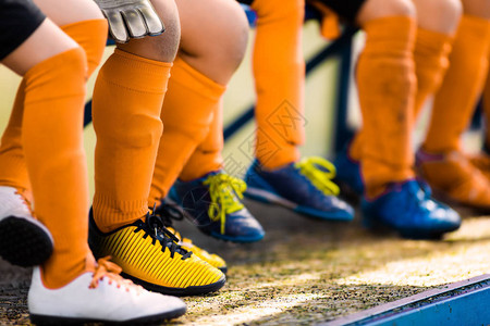 护腿穿着足球鞋的足球运动员穿着足球服的青年运动员穿着足球衣服和足球鞋的年轻足球运动员连续坐在长凳上背景
