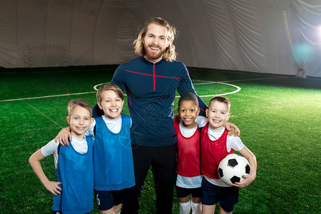 成功的足球教练和4名穿着制服的快乐男孩站在绿色图片