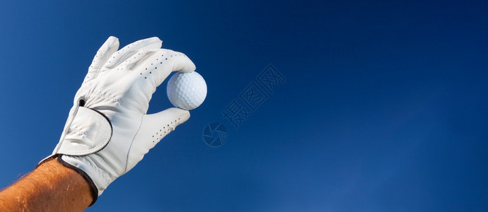 戴高尔夫手套的手拿着白色高尔夫球在深蓝色天空上图片