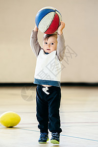 可爱的小白人幼儿男孩在纯白光背景下在健身房打篮球图片
