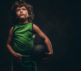 小篮球运动员穿运动服在演播室里拿着球被暗色背景图片