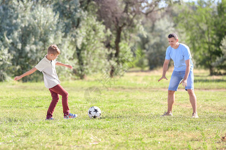 小男孩和他爸在户外踢足球图片