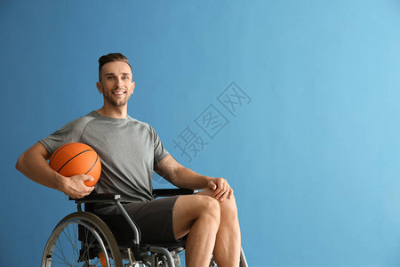 年轻篮球运动员在彩色背景下坐在轮椅上的青图片