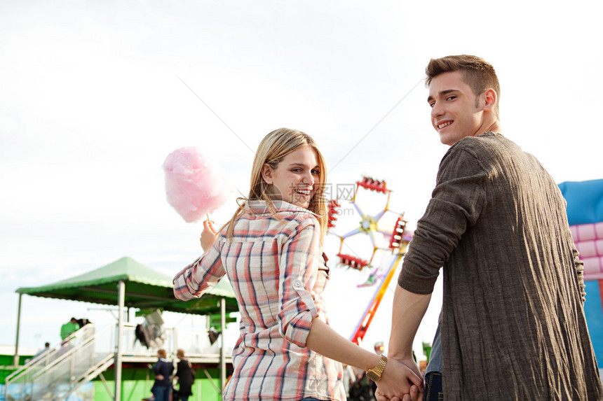 有魅力的年轻夫妇握着手在公园街游乐场玩得开心拿着棉花糖甜的转而图片
