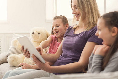 快乐美丽的女人和她迷人的小女儿坐在家里的沙发上玩数字平板电脑租图片