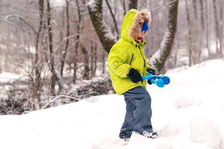 穿着保暖衣服的可爱小男孩在冬季公园用制造商玩具滚雪球冬季家庭度假降雪背景图片