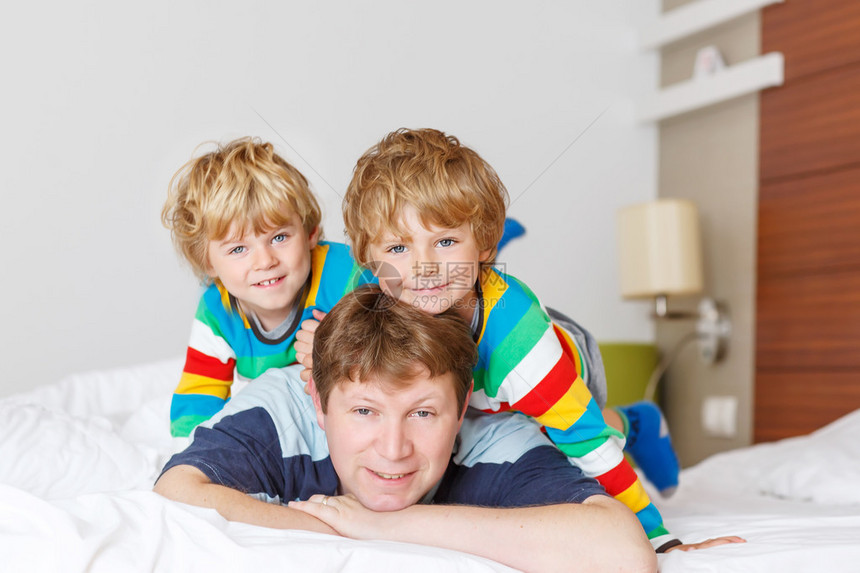 两个小兄弟男孩和他们的爸在家睡觉后在床上玩得很开心图片