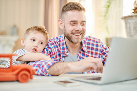 快乐的留着胡子的男人穿着格子衬衫和他可爱的小儿子在家里度过周末时一图片