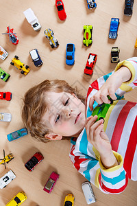 有趣的小男孩在室内玩具车小孩男穿多彩的衬图片