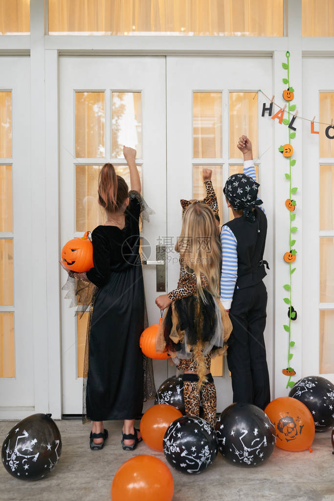 孩子们穿着漂亮的万圣节服装站在房子的门廊上敲门要图片