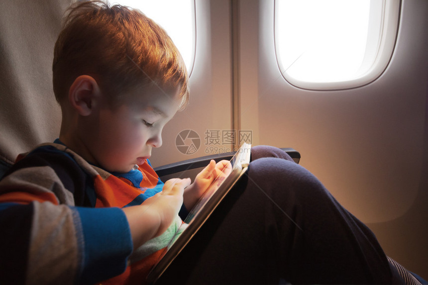 小孩膝盖上有平板电脑坐在飞机上的发光机图片