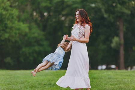 快乐的女人穿着轻便的衣服和可爱的小宝贝女孩在公园的绿草坪上玩耍图片