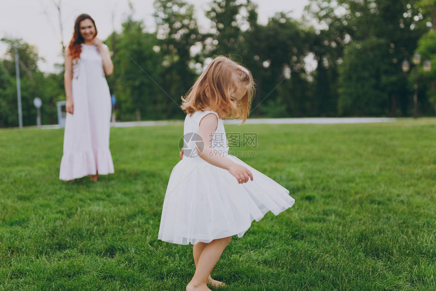 漂亮可爱的小宝贝女孩穿着轻便的衣服在公园的绿草坪上转圈图片
