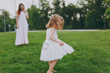 漂亮可爱的小宝贝女孩穿着轻便的衣服在公园的绿草坪上转圈背景图片