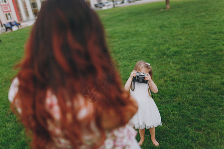 穿着轻便衣服的小女孩在公园绿草上用复古老式照片相机给妈拍照图片