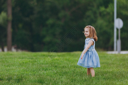 漂亮可爱的小女孩穿着牛仔裙站在公园的绿草坪上玩耍和玩乐图片