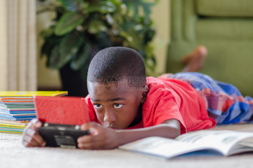 一个年轻的非裔美国男孩躺下玩游戏图片