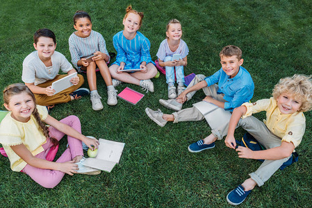 坐在草地上带书本和器械的快乐学童群体图片