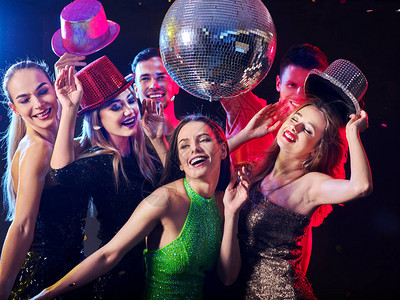 与一群人跳舞的会女人和男人在夜总会玩得很开心前景的快乐女孩和背景的迪斯科舞会伙计们脱下帽子辛苦工作一背景图片